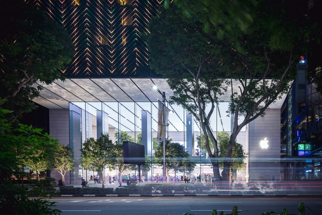 office_building Night view of a modern, glass-fronted office building, surrounded by trees and located in an urban area, with illuminated interior and people inside, set against the backdrop of city lights and buildings.